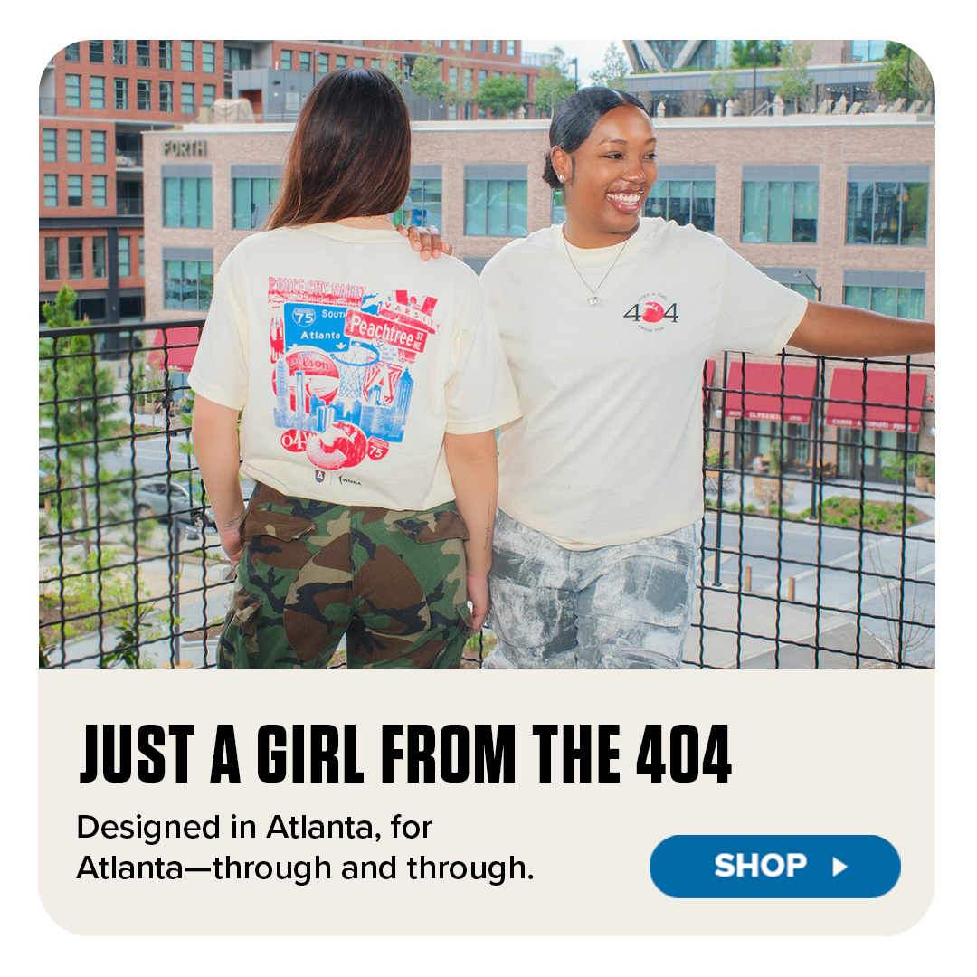 Two women wearing cream-colored "Just a Girl from the 404" Atlanta-themed t-shirts stand on a city rooftop, smiling and enjoying the view. One shirt features bold, colorful Atlanta graphics on the back, while the other shows a front chest logo. The image promotes locally inspired apparel with the tagline “Designed in Atlanta, for Atlanta—through and through,” and includes a “Shop” button.